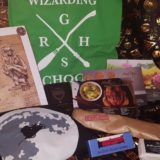 Geek Gear July 2018: Demiguise print, Slytherin tote bag, Slytherin Quidditch Captain’s pin, Hagrid silhouette T-shirt, magical steam engine miniature, butterscotch soap, wizarding world recipe cards, and wand wrapped in parchment paper