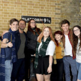 A group of fans from all the Houses poses with Law and Redmayne at Platform 9 3/4.