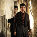 Credence and the Maledictus peer through hanging fabric.