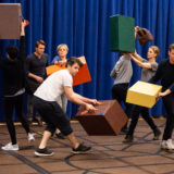 Cast members practice moving luggage around the “stage.”