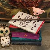 Harry Potter: Manage Your Mischief Marauder’s Map Sequin Notebook alternate cover, displayed on top of a stack of “Harry Potter” books with wand, Dobby figurine, and owl
