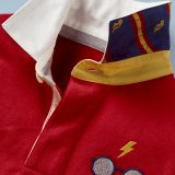 This close-up of the Mini Boden Hogwarts Rugby Shirt in red provides a better look at the collar design and glasses-and-scar logo in the front pocket area. It retails at £30.