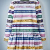 The Mini Boden Charms Class Stripe Dress, multi-color, features alternating white and colored stripes. The colored stripes include spell incantations separated by lightning bolts, including “Wingardium Leviosa,” “Riddikulus,” “Expelliarmus,” and “Lumos.” It retails at £28.