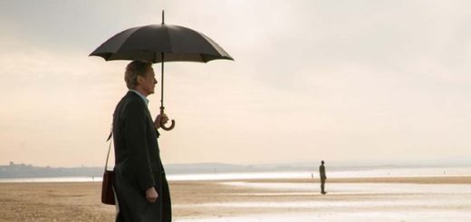 Bill Nighy stands on a beach under a black umbrella looking contemplative in Sometimes, Always, Never.