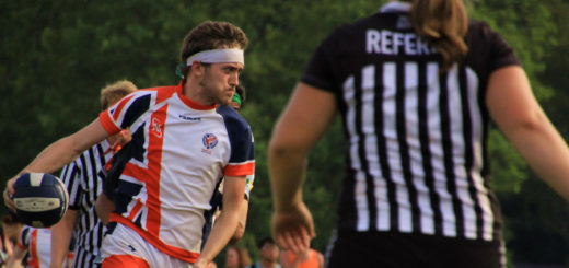 A chaser from the United Kingdom is holding a quaffle. There is a referee on the right and another referee in the background.