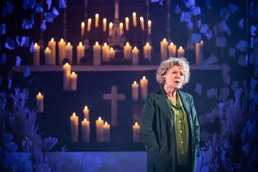 Imelda Staunton recites her lines in front of a backdrop of candles and a cross in a still image from the Donmar Warehouse’s holiday production. (Credit: Save the Stage/Donmar Warehouse’s)