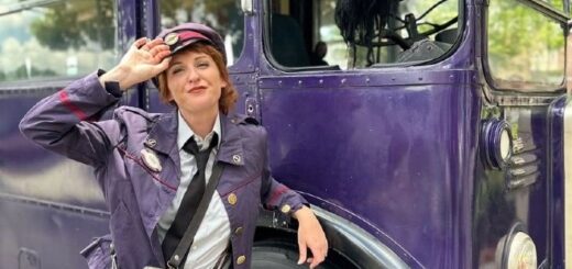 The Knight Bus Conductor tips her cap while leaning on the front wheel.