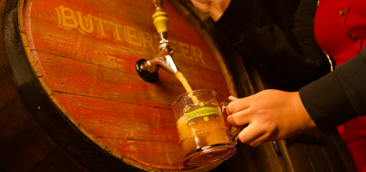 A hand holding a glass stein filling it with Butterbeer at a barrel